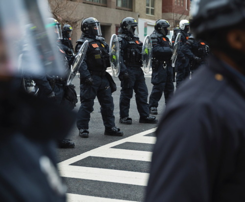 Police in riot gear are lined up outside a city building.