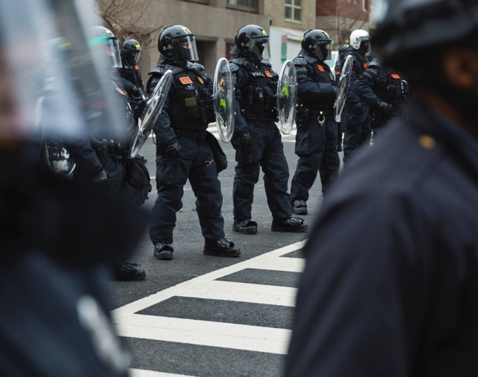 Police in riot gear are lined up outside a city building.