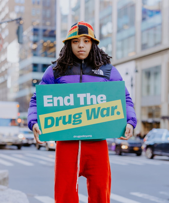 A young woman holds a sign that says "End the Drug War."