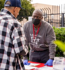 A man from a health intervention program talks with someone at a table at an outreach fair.