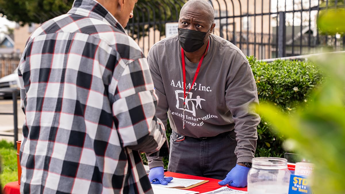 A man from a health intervention program talks with someone at a table at an outreach fair.