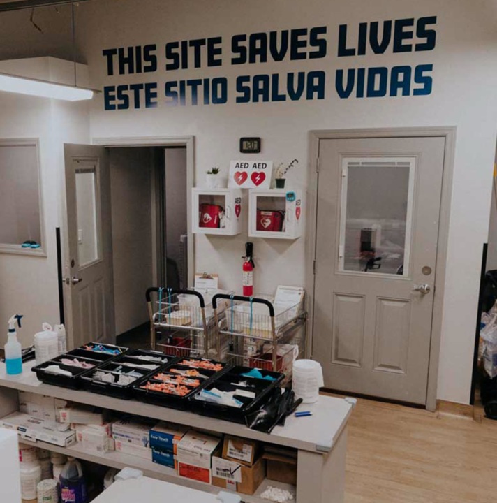 Interior of OnPoint NYC overdose prevention center. The wall reads "This Site Saves Lives" in English and Spanish.