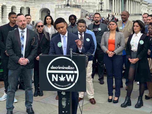 Photo of DPA Staff Cat Packer giving a speech at a podium labeled "Deciminalize Now 4/20 Unity Day of Action". There is a small crowd behind the speaker.
