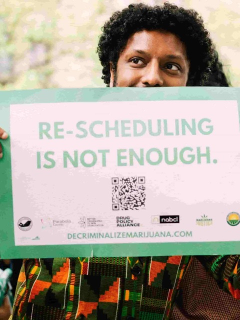Photo of man holding a sign that says "Re-scheduling is not enough. decriminalizemarijuana.com"