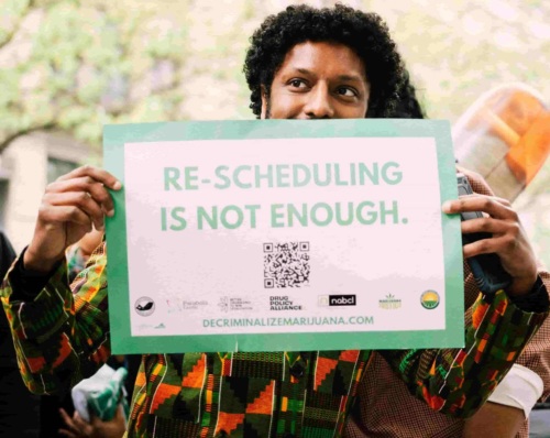 Photo of man holding a sign that says "Re-scheduling is not enough. decriminalizemarijuana.com"